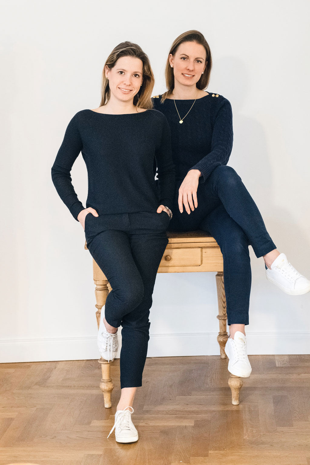 Foto von zwei Frauen, die an einem Sekretär lehnen. Zu sehen sind: Katharina Konrad & Anna Lina Schuhmacher, beide Creative Art Director der DEBA GmbH.