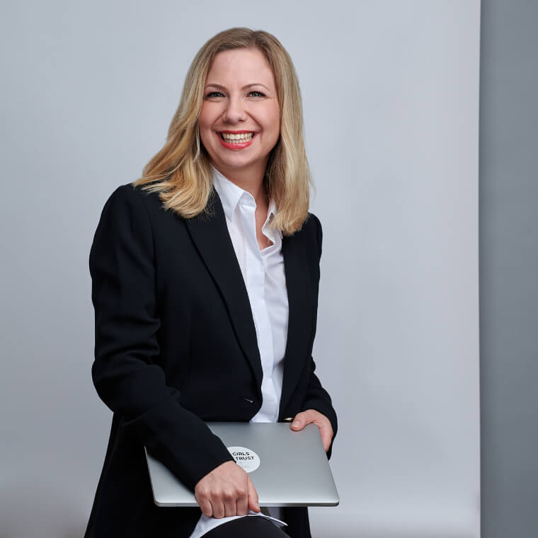 Foto einer lachenden blonden Frau, die ein MacBook in ihren Händen hält. Zu sehen ist: Judith Plawilm, Corporate Communications Managerin DEBA.
