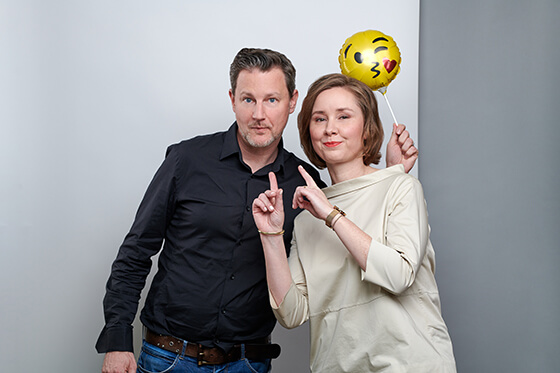 Foto von einem Mann in einem dunklen Hemd neben einer Frau mit heller Bluse. Der Mann hält einen Emoji-Ballon in der Hand. Die Frau zeigt mit beiden Zeigefingern auf den Mann. Zu sehen: Wolf Reiner Kriegler (Founder & CEO DEBA) sowie Petra Fellmann (Lead Corporate Communications & Community DEBA).