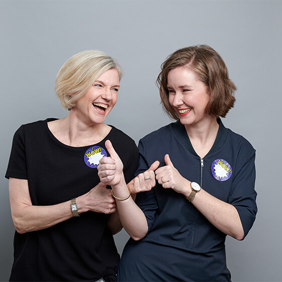 Foto zweier lachender Frauen mit dunkler Kleidung und Bobfrisuren vor grauem Hintergrund. Zu sehen: Susanne Siebrecht (Associated Consultant DEBA) und Petra Fellmann (Lead Corporate Communications & Community DEBA).