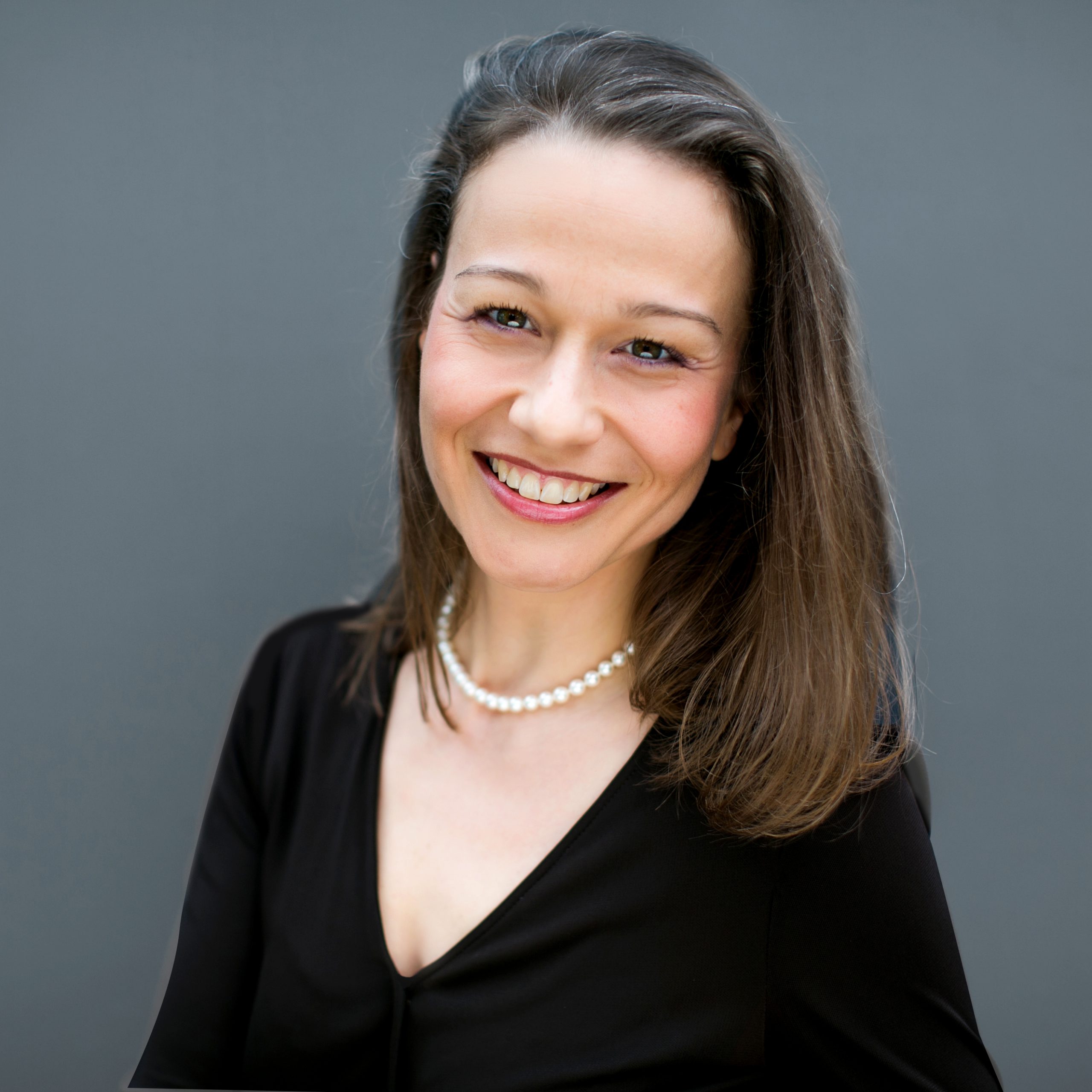 Portraitfoto einer lachenden. brünetten Frau, die ein schwarzes Oberteil und eine Perlenkette trägt. Zu sehen ist: Bettina Helfenstein - Associated Consultant DEBA.